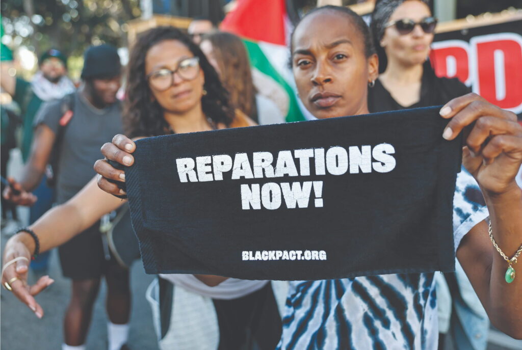A protester displays a sign reading "Reparations Now!" during a May 21 rally in Los Angeles billed as a “Day of Resistance” against the resurgence of racism in the United States. In October, California Gov. Gavin Newsom vetoed several reparations bills, including two that would have given descendants of enslaved people preferences in college admissions and aid for first-time home-buyers. 